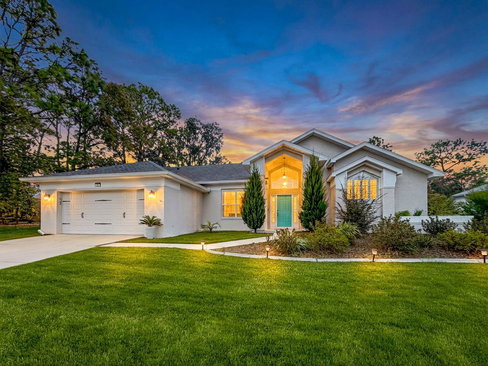 Beige single-story home at 11 Maidenbush Ct E at dusk with a teal arched entry and a two-car garage